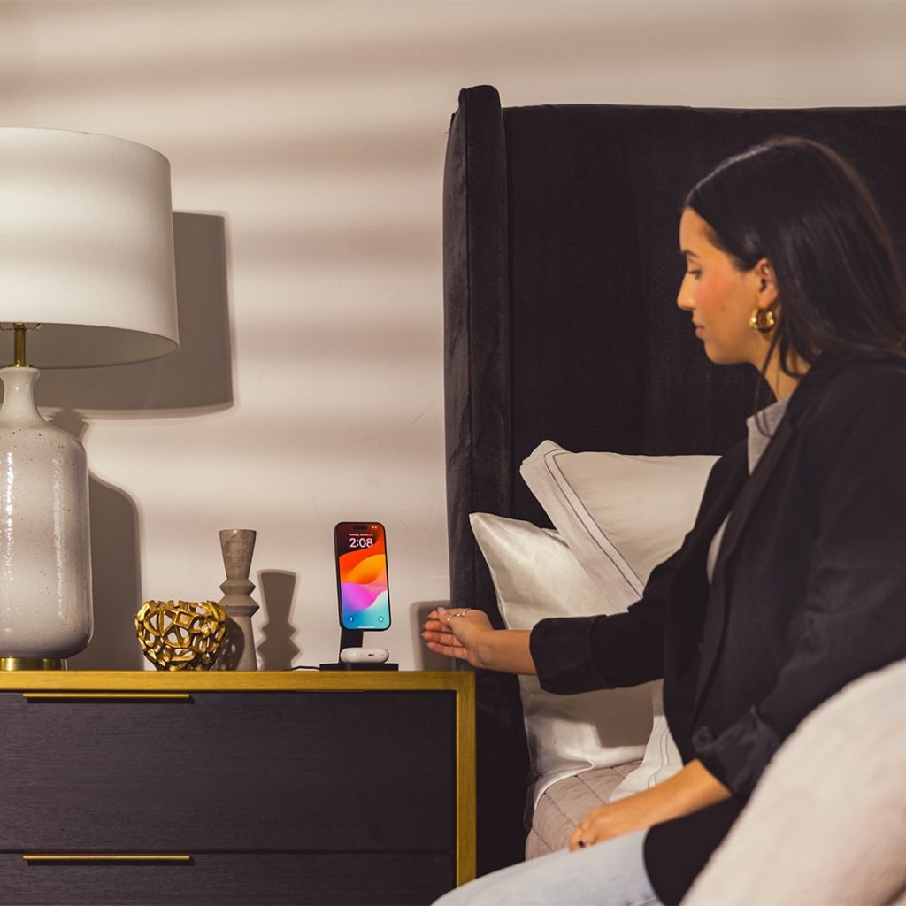 woman sitting on bed with mophie phone stand on night stand
